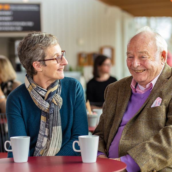 A woman and a man of different ages sit together chatting happily over a cup of tea in our cafe.