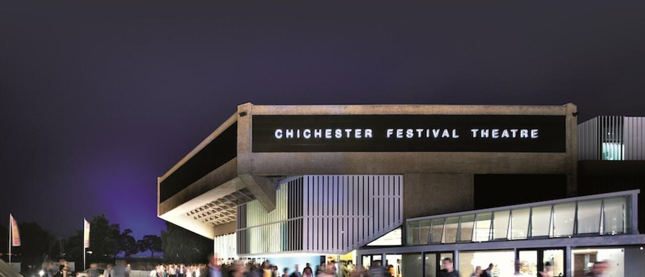 The outside of the Festival Theatre at night time. The building is lit and there is a blur of people moving around outside.