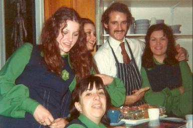 Five CFT staff members in green uniforms and blue aprons smile at the camera in a vintage photo.