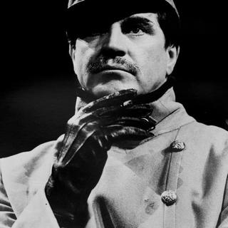 A close up of the actor Alan Bates wearing a hat, military uniform and gloves