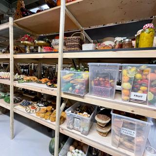 Clear plastic crates filled with artificial fruit, bread and pastry, cakes and sweets, and platters of artificial food including roast chicken, canapes and pork pies, and jars filled with fake pickle and jams