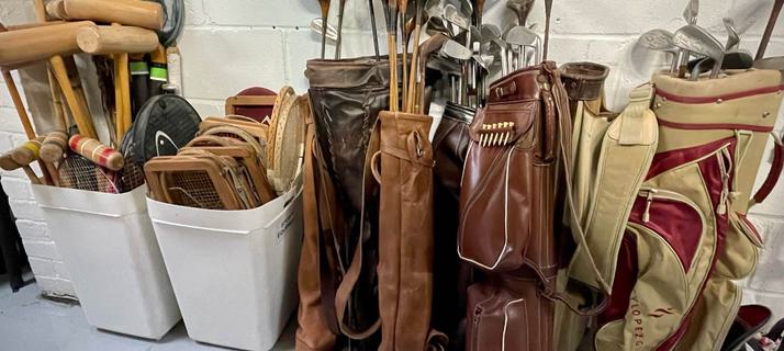 Several sets of golf clubs in brown leather and canvas bags, collections of vintage tennis rackets, croquet mallets and fishing nets stored in white plastic bins