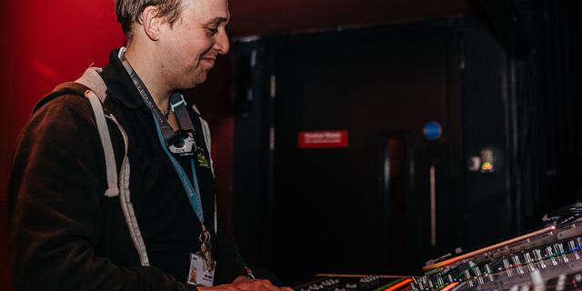 A man stands over a sound desk, smiling