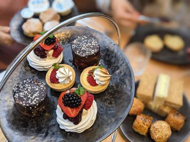 Afternoon tea on a tiered platter - close up of mini cakes on a grey plate and sandwiches and scones in the background.