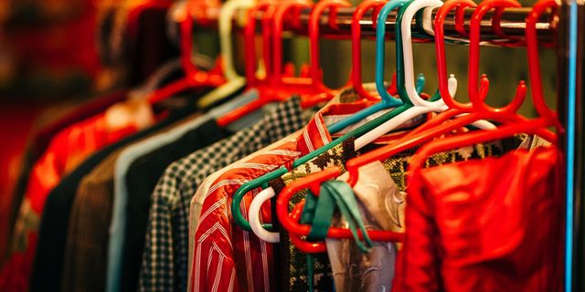 A clothing rack with colourful red, white and green hangars, it holds a row of Santa's clothes. In focus there is a pair of folded red trousers, a stripy red shirt, and a checked green and white shirt.