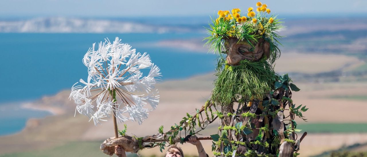 A beautifully crafted 8-foot puppet Daniel, an ethereal, ancient man of the earth, walks holding a larger than life dandelion.