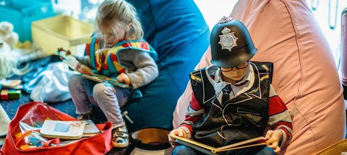 Two children in fancy dress sit on colourful beanbags while busy reading. Books and toys are on the floor around them.