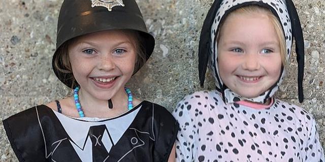 Two girls look directly into camera smiling; they are wearing fancy dress of a police officer and a dalmation.