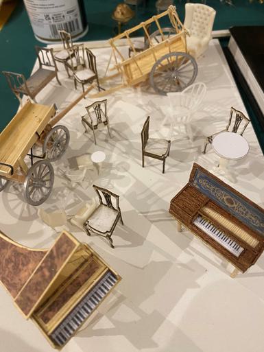 Models of miniature chairs, two miniature carts and two miniature pianos on a piece of white paper.