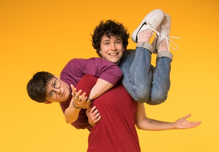 A girl clings to her friend horizontally, the other stands with her hands outstretched