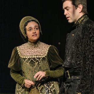 A man and woman both in traditional Tudor costumes stand close to each other looking unhappy