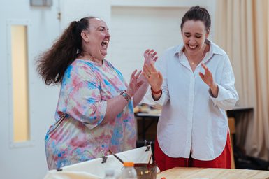 Two women are stood laughing joyously with one another.