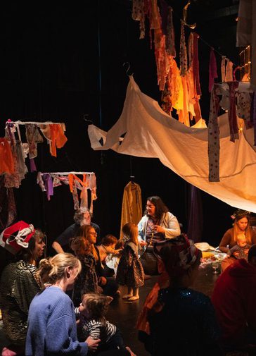 Parents and children in a dark tent like space; atmosphere warm lights illuminate colourful bunting.
