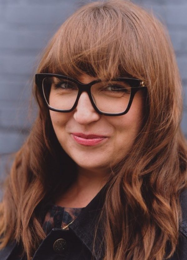 A portrait of a smiling women with big glasses and long dark hair.