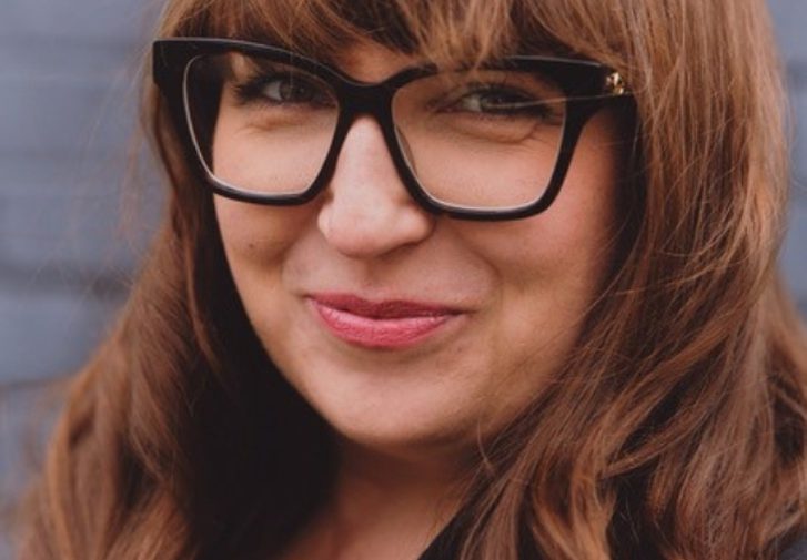 A portrait of a smiling women with big glasses and long dark hair.