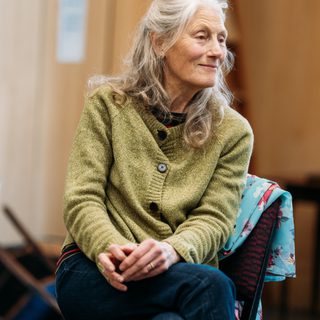 An actress leans forward on a chair, she smiles wistfully.