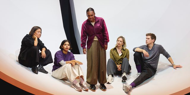 Five performers are inside a huge, white hemisphere, with a black slit through the middle, suspended above the ground. A young woman in the centre stands and speaks passionately, looking at something beyond the camera. Three of the others watch her, whilst the forth also looks out into the distance, hopefully. They wear stylish, casual clothes.