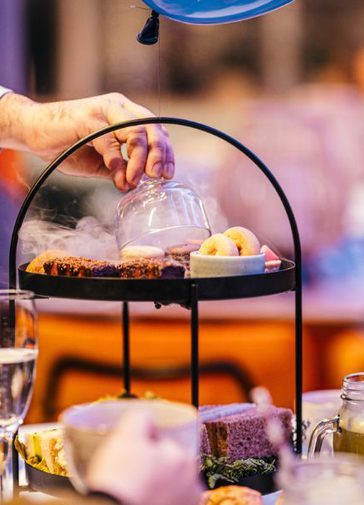 A man's hand is revealing a delicious delight on on Afternoon Tea on tiered plates