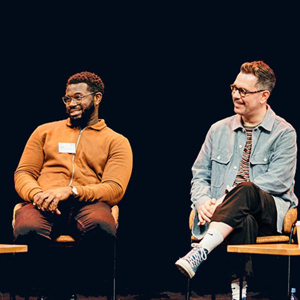 Three men and one woman, of different ages, dressed in casual clothes are sat on our stage holding microphones. One person is talking into the microphone while the others listen