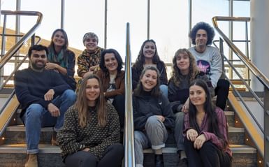 A group photo of people seated on the stairs inside the Minerva Theatre foyer. They are all facing the camera and smiling happily.