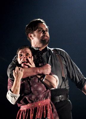 Sweeney Todd (Michael Ball) holds Mrs Lovett (Imelda Staunton) roughly with a cut throat razor in his hands. She looks terrified and he gazes menacingly into the distance.