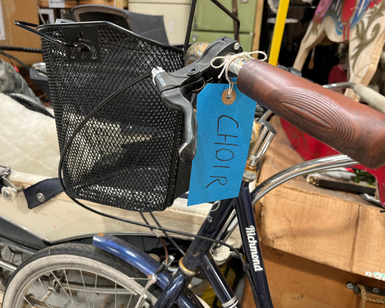 A close up of a basket and handlebars on a bike, with a blue label that reads 'Choir' attached.