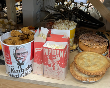 A selection of props mimicking food: a bucket of fried chicken, boxes of popcorn and some pies.