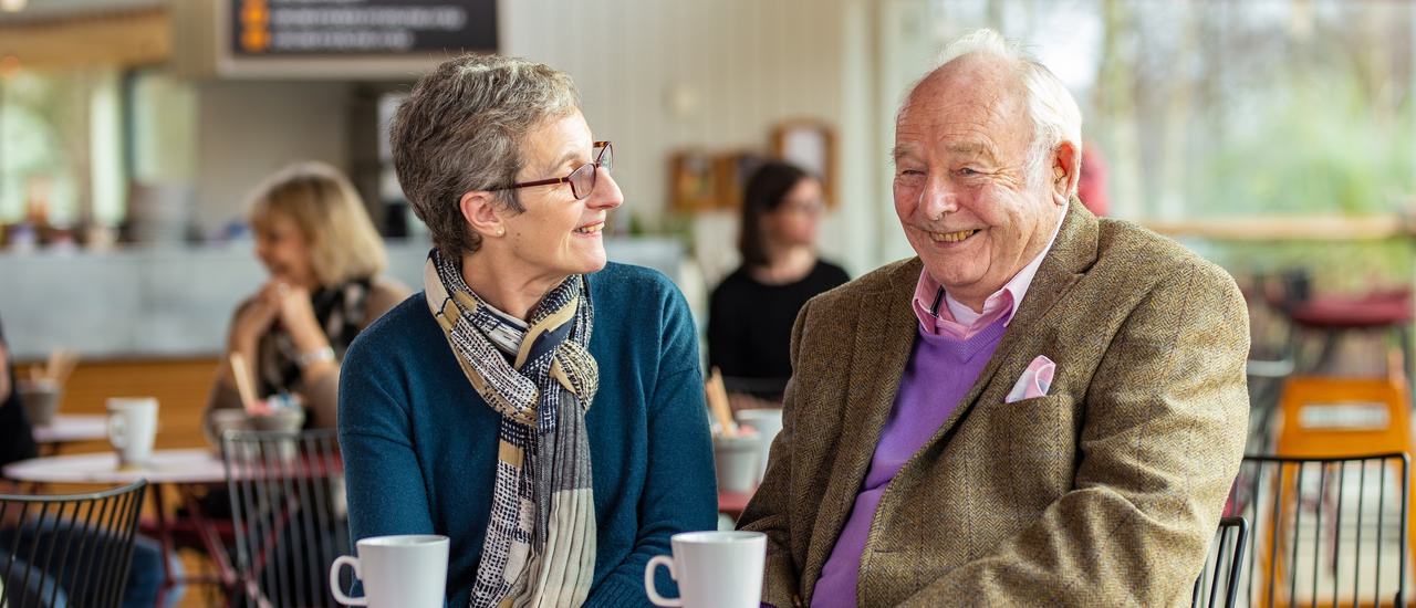A man and a woman sitting together in our café enjoying a cup of tea and laughing together