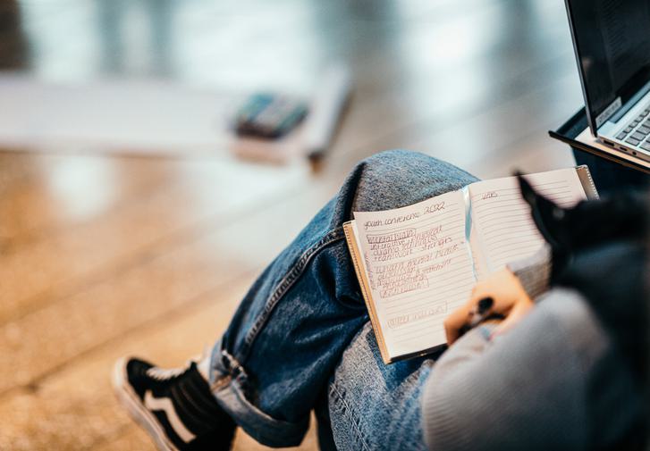 Person wearing jeans sitting down with an open notebook and pen in their lap.