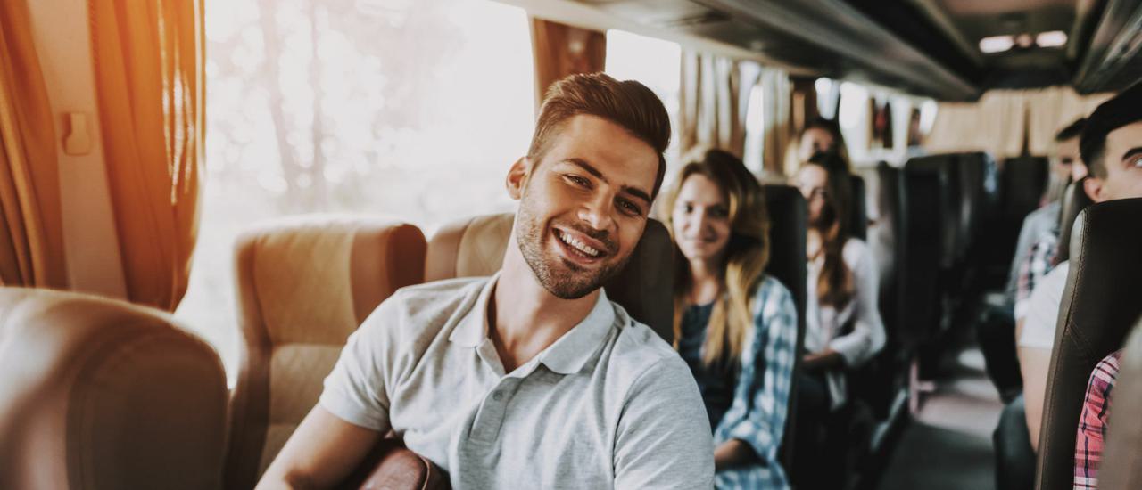 A smiling man is sat on a busy bus.