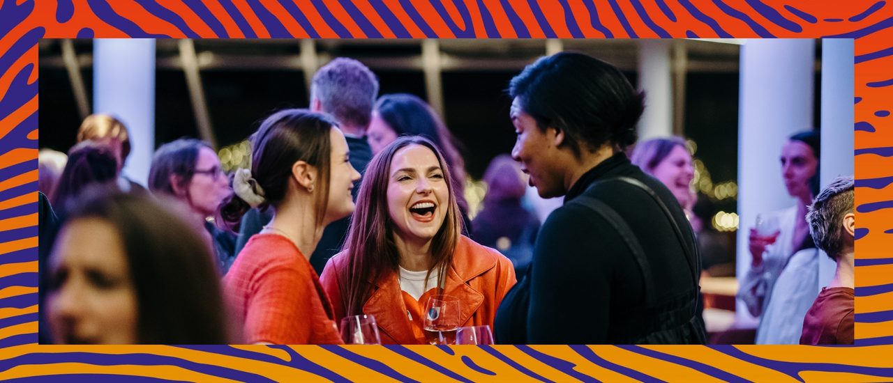 A group of friends making each other laugh in the Minerva bar. The image has a blue and orange thumbprint border.