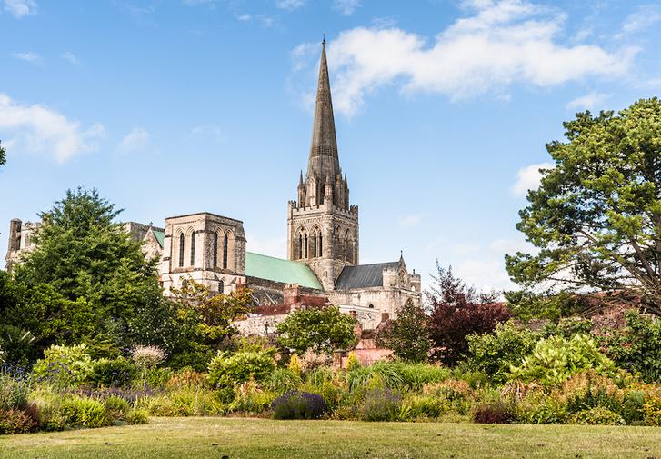 Chichester Cathedral seen from the lawns of the Bishop's Palace Gardens. The cathedral can be seen through the shrubs and trees