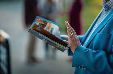 A man in a blue jacket reads a programme.