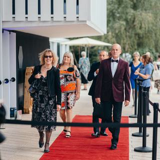 Men and women in evening dress and black tie approach the theatre across a red carpet.
