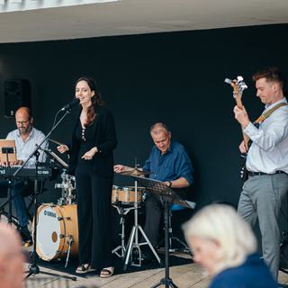 Four musicians - a female vocalist in the centre, with three men on keyboard, drums and guitar, play outside CFT.