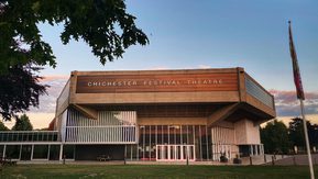 The Chichester Festival Theatre building with a sunset in the background.