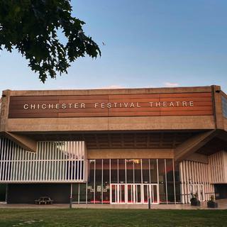 The Chichester Festival Theatre building with a sunset in the background.