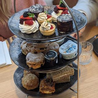 The top of three tiers of afternoon tea stand with beautiful selection of cakes, with sandwiches, sausage rolls and scones underneath..