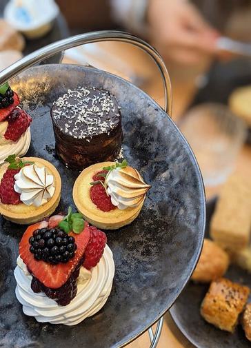 The top of three tiers of afternoon tea stand with beautiful selection of cakes.