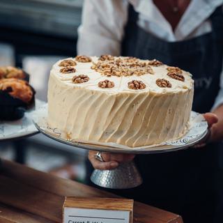 A waitress places a large (delicious) coffee and walnut cake on a stand onto the cafe counter.