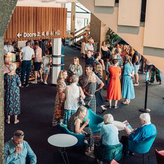 The Festival Theatre foyer is full of people, some sitting, some standing and some waiting for drinks at the bar.