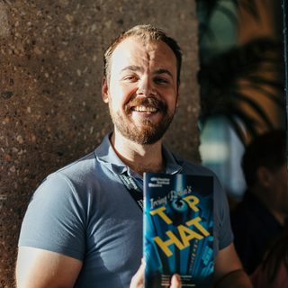 A front of house assistant holds a programme for Top Hat and smiles at the camera