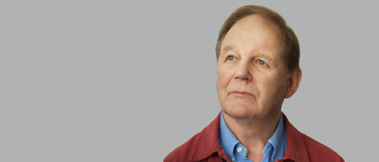 Michael Morpurgo (a white man with grey hair in a blue shirt and red jacket) looks wistfully to the left