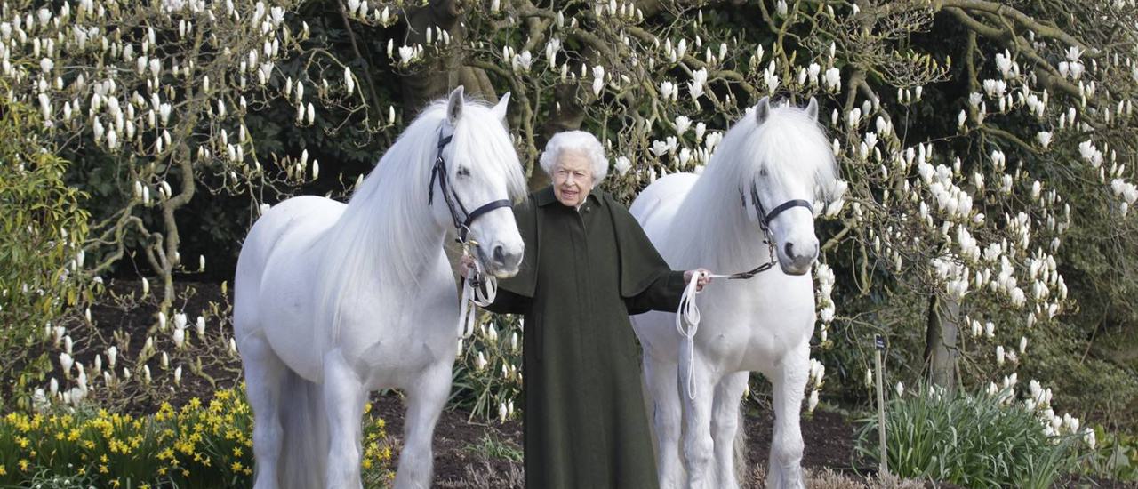Her Majesty standing in between two of her fell ponies, Bybeck Katie and Bybeck Nightingale, on the grounds of Windsor Castle. She holds the reins of her ponies while dressed in a deep moss green coat.