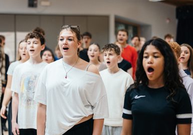A group of young performers are stood in rows singing.