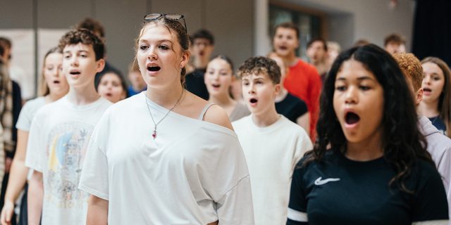 A group of young performers are stood in rows singing.