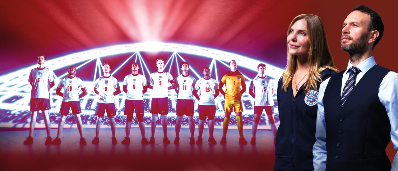 A man and a woman stand beside one another, proudly looking up into the distance. The woman (labelled Samantha Womack as Pippa Grange) wears an England football team tracksuit with the three lions badge. The man (labelled David Sturzaker as Gareth Southgate) wears Southgate's iconic waistcoat over a shirt and tie. The red background features an illuminated stadium with England football players lined up proudly in front of it. Text over the image reads: 'Five stars (The i), 'The decade's biggest theatrical triumph' (Telegraph). The acclaimed National Theatre production: Dear England. A new play by James Graham, directed by Rupert Goold, set design by Es Devlin.'