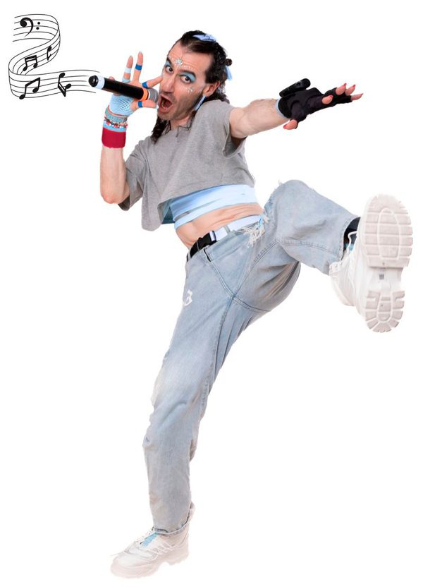 A performer wearing distressed light blue jeans, a cropped grey t-shirt, black fingerless gloves and chunky black boots stands on one leg, with the other leg kicking out in front of them. They look at the camera and speak into a microphone, with a graphic of musical notes coming out of it.