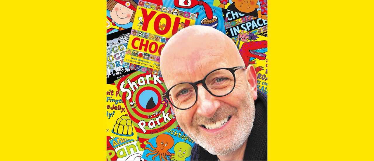 Nick Sharratt, a bald man with black, round glasses, smiles warmly with a collage of brightly coloured illustrated picture book covers in the background.