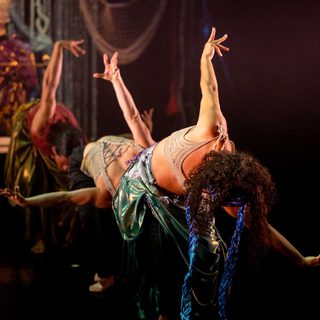 Three dancers are bent over at the waist with their arms extended away from their bodies.